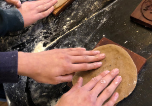 Dłonie uczniów ugniatają oraz formują koła z ciasta piernikowego.